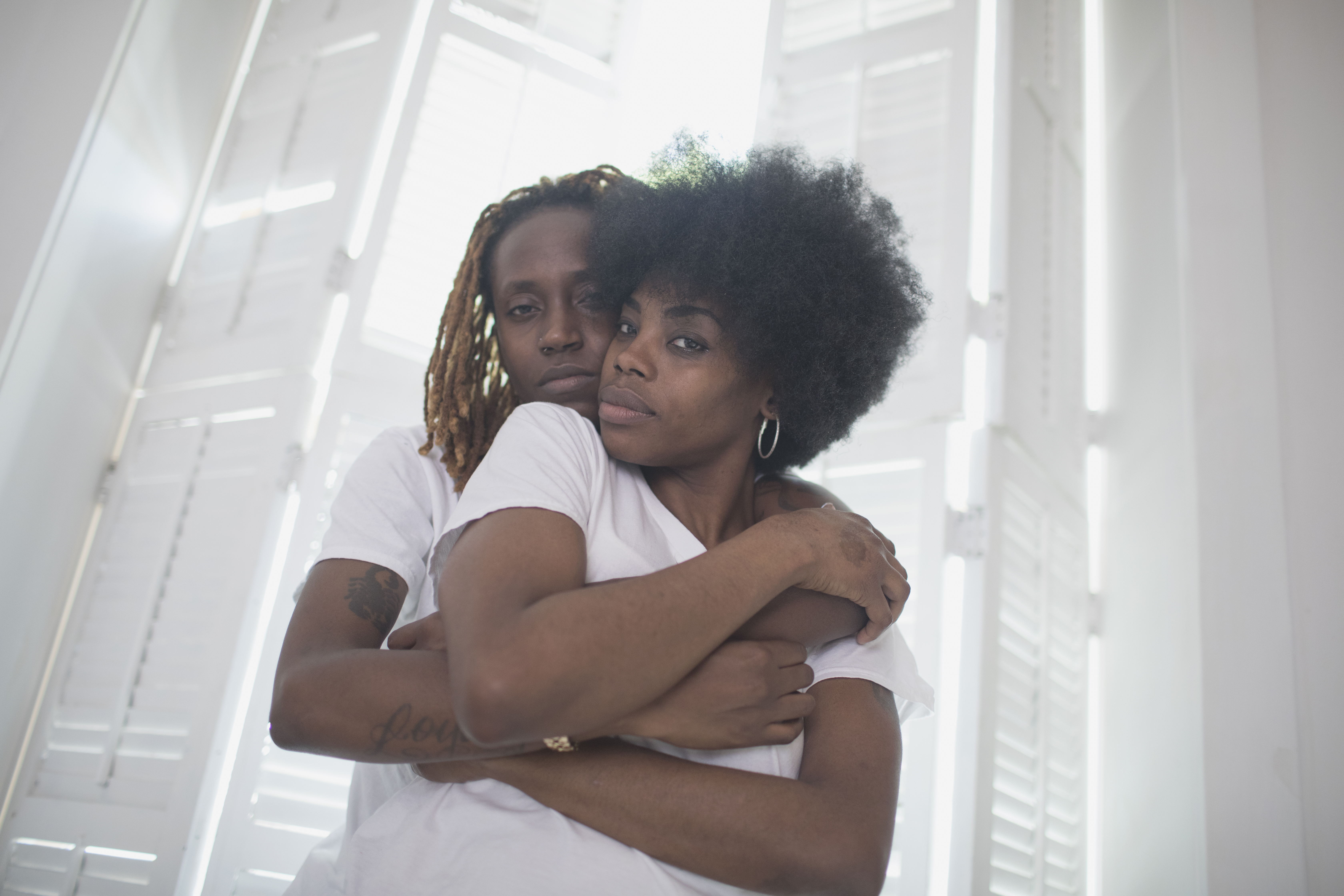 Lesbian couple embracing beside a window with shutters