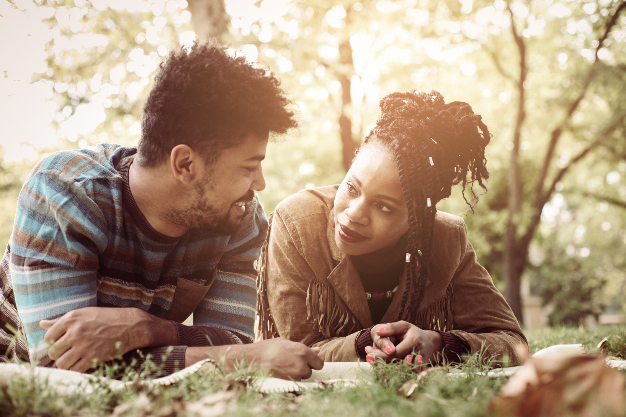 Happy African American couple lying down and in park and having conversation.