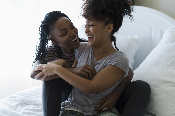 Lesbian couple relaxing on bed, hugging, laughing