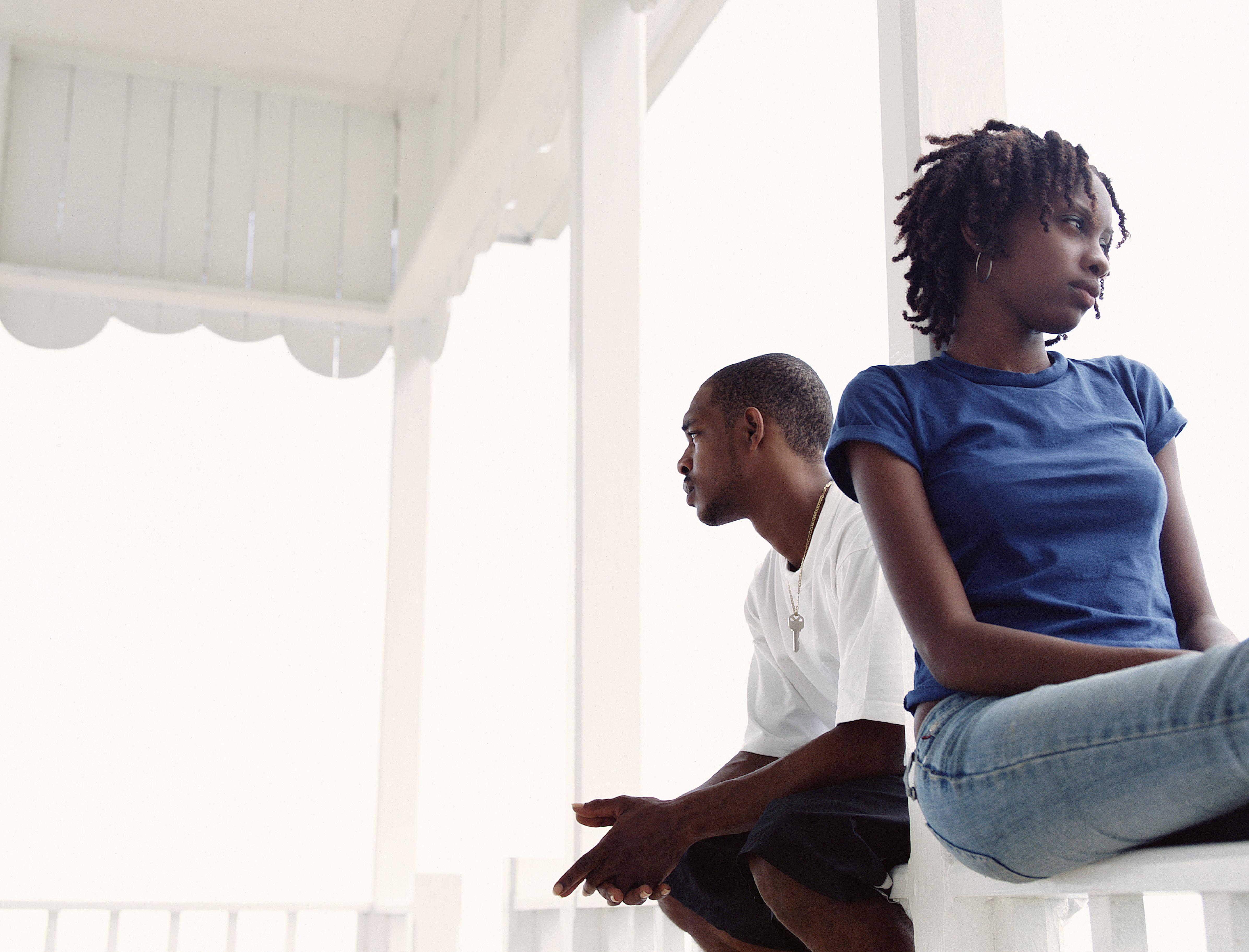 Couple relaxing on veranda, sitting on rail with backs to each other