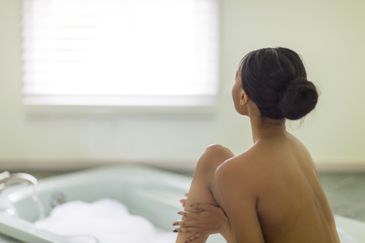 Naked young woman in bathroom gazing through window, solo Valentine’s Day