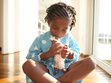 Girl (3-5) kissing doll on floor, close-up