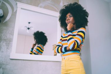 African woman standing pensive in front of a mirror