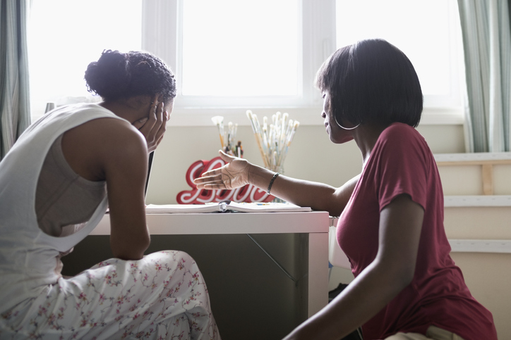 Mother helping teenage daughter with homework at desk in bedroom