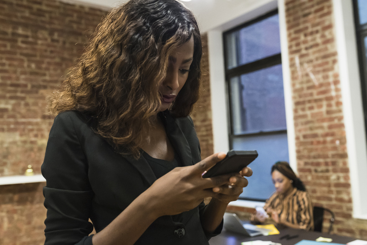 Businesswoman texting, colleague using laptop in background