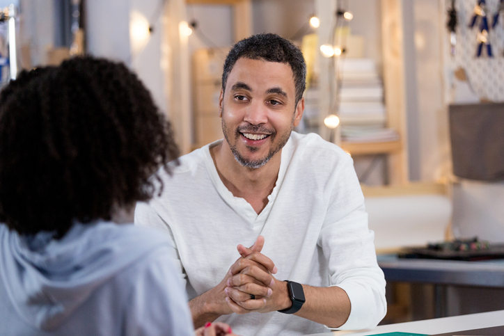 Mid adult dad clasps hands in chat with unrecognizable teen