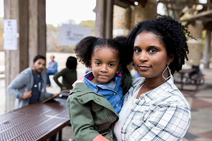 Mid adult single mother holds young daughter at free clinic