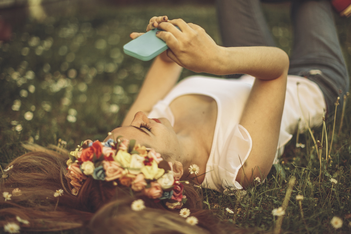 Young girl is lying in the grass and taking selfies