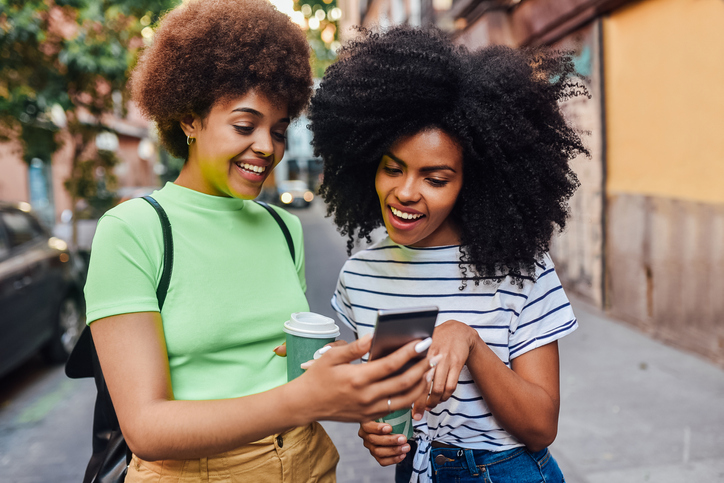 Two girls waiting for a taxi and using smartphone