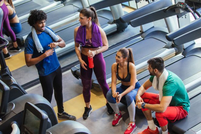 Young cheerful people resting from exercising at gym and communicating