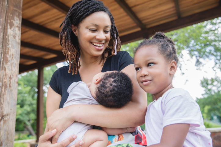 Mother smiles at toddler daughter while holding infant son