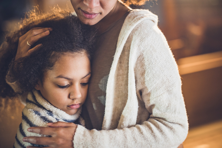 Sad African American girl embracing her mother at home.