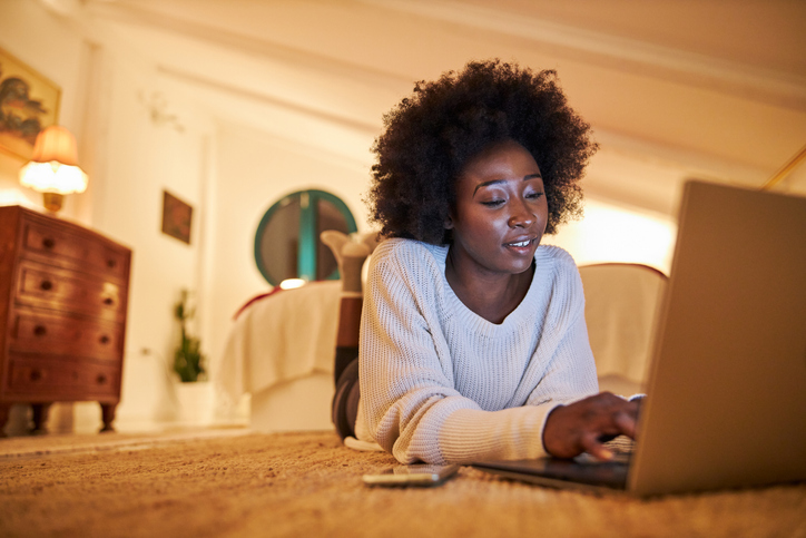 A young black woman working on her laptop in her bedroom.