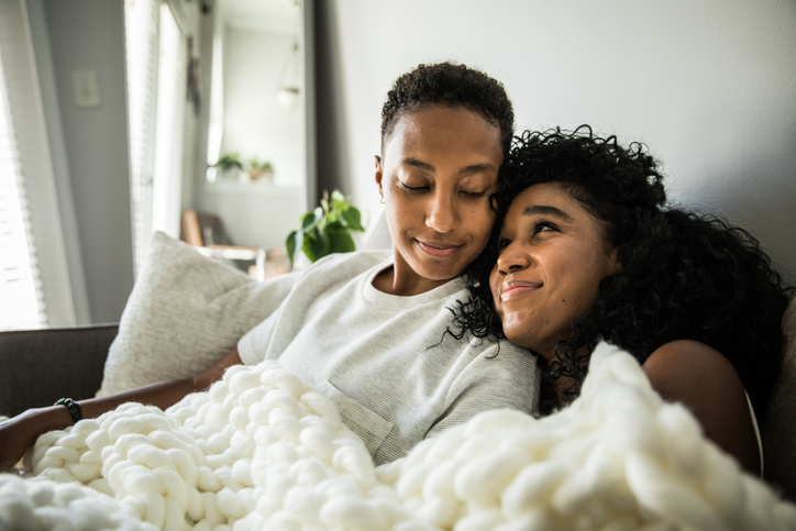 Lesbian couple at home snuggling under blanket