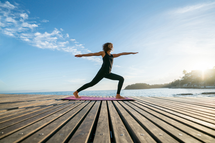 Woman meditating outdoors wearing facemask at a pier