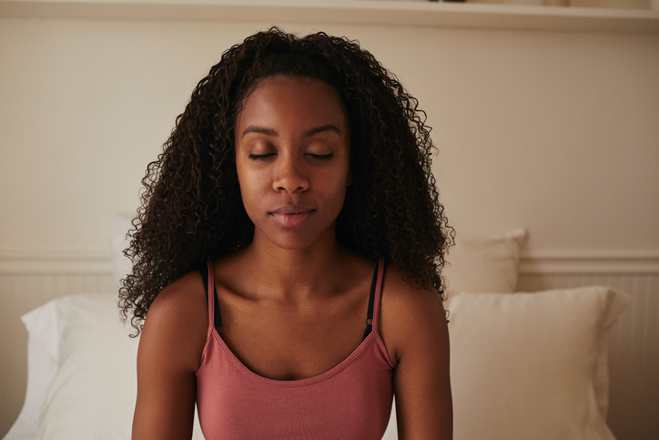 Young woman sitting on her bed with her eyes closed