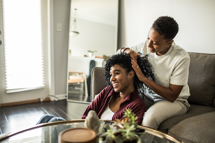 Woman brushing girlfriend's hair on couch