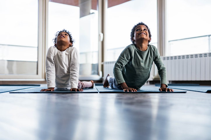 Happy African American siblings stretching on exercise mats at home.
