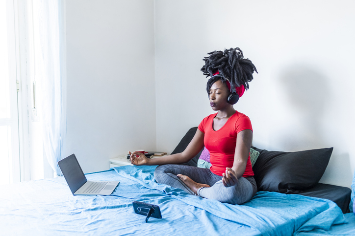 Young woman meditating at laptop sitting on bed