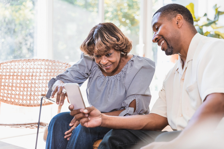 Mid adult son shows senior mother grandchildren pictures on tablet