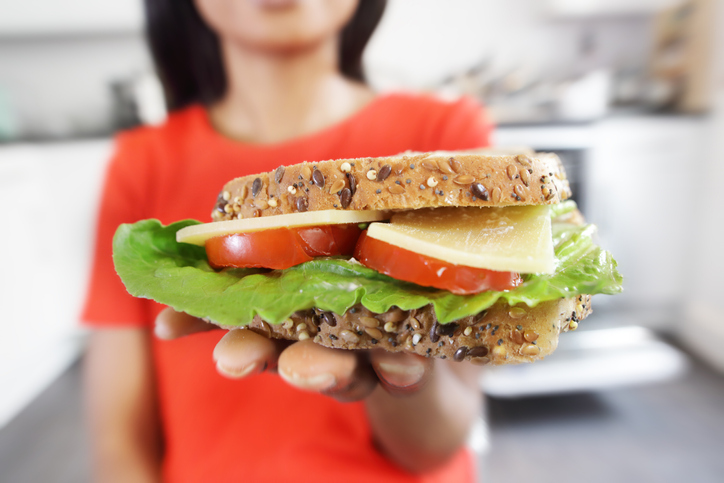 Young woman eating cheese and salad sandwich at home