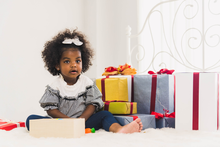 Full Length Of Girl Holding Gift Sitting On Bed At Home