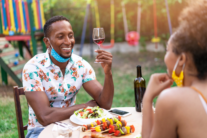 Afro Couple wearing protective face mask having staycation romantic dinner on back yard, during COVID-19