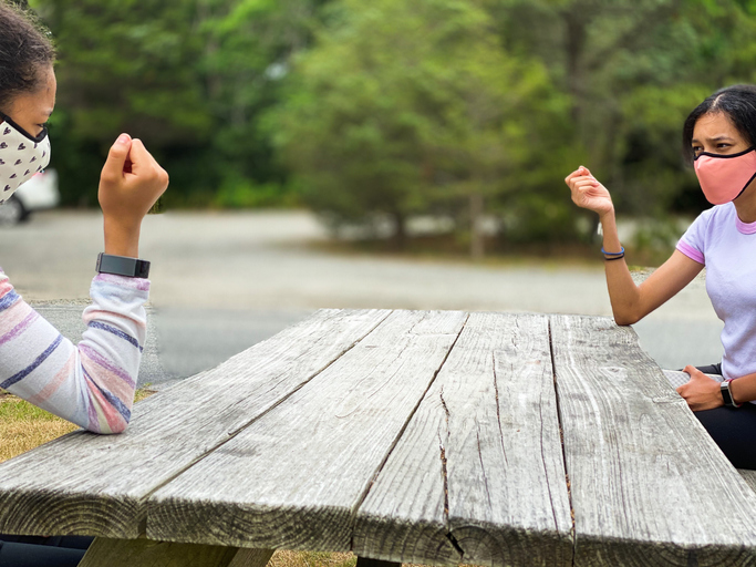 two mixed-race teen girls have a tense socially-distanced conversation sitting on opposite sides of picnic table