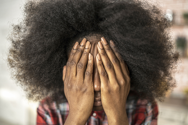 African woman sitting at home hands on face stock