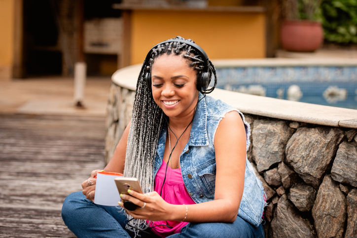 Black woman using cell phone and headphone outdoors in the back yard