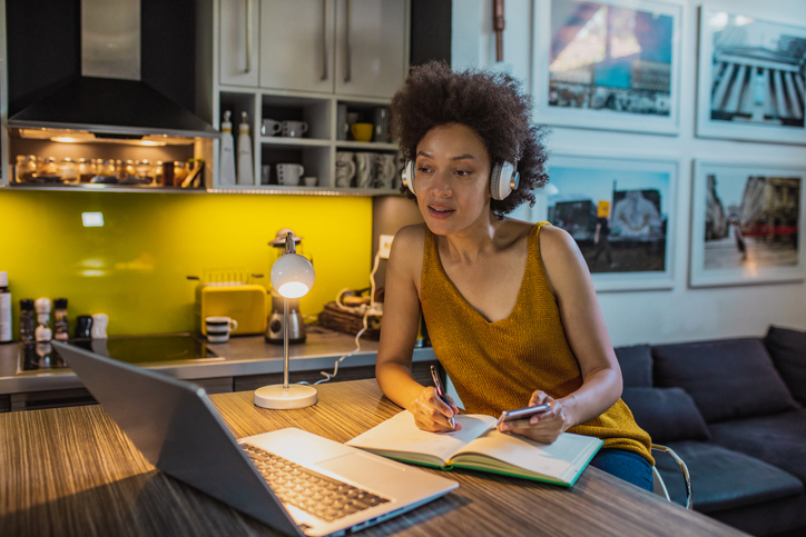 African American woman with headphones is working from home on laptop