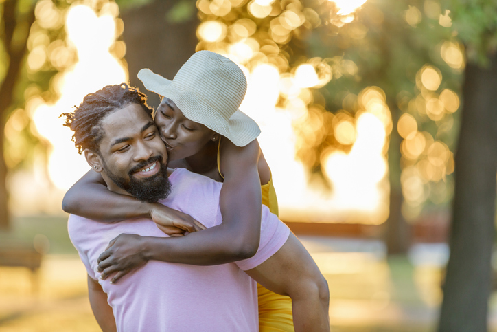 Young African-American Man is Carrying his Lovely Wife on Piggyback in the Public Park.
