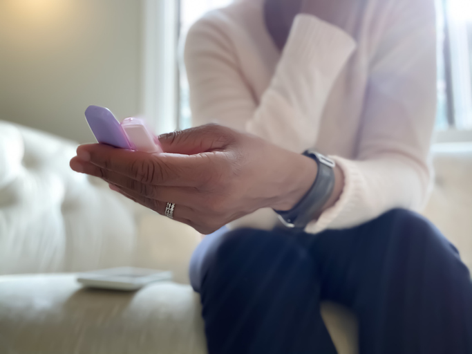 african-american woman reads results of two home pregnancy tests while sitting on couch with mobile phone nearby