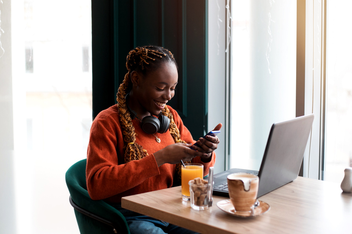 Close-up portrait of young african woman using smartphone in cafe.