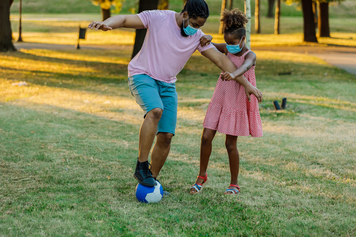 A Happy African-American Father and Daughter are Enjoying Outdoors and Playing With Soccer Ball in the Time of Corona Virus.