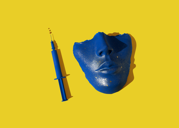 Blue colored syringe and face/ mask on the yellow background.