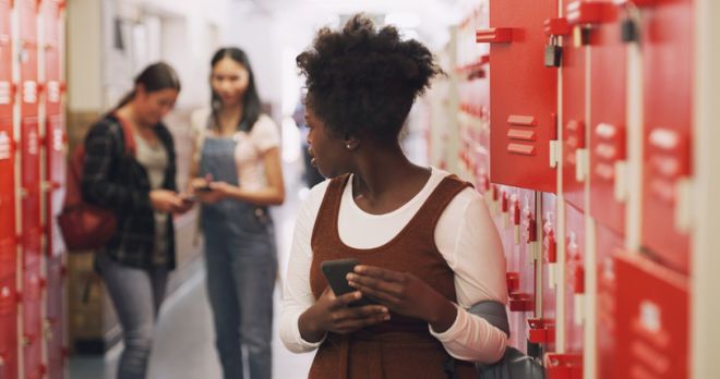 Shot of a teenage girl using a smartphone next to her locker and being bullied at high school