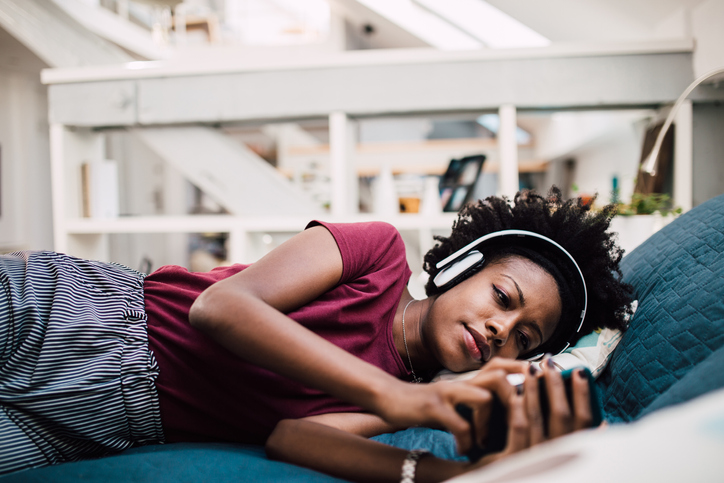 Beautiful African-American woman relaxing in her bed and podcasting