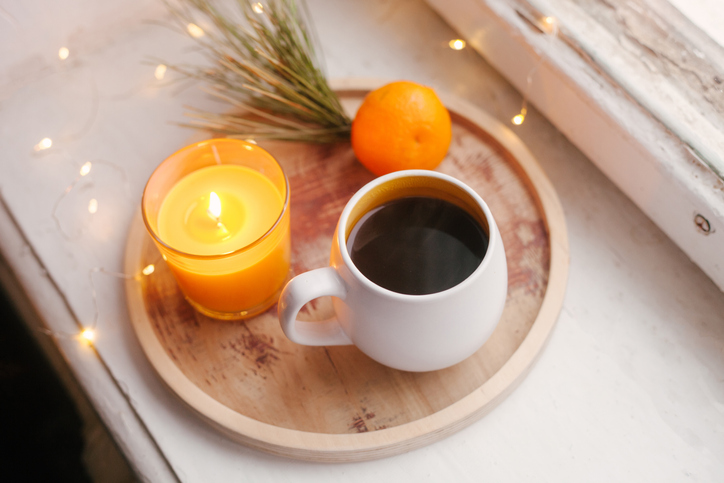 Cozy winter home interior details, cup of coffee, wooden tray, tangerine and candle. Window sill. Still life for Christmas.
