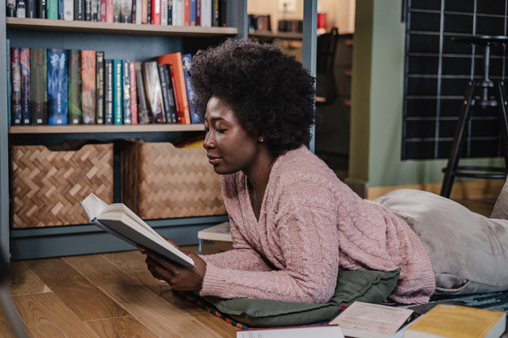 Young African-American woman reading a book at home on the floor