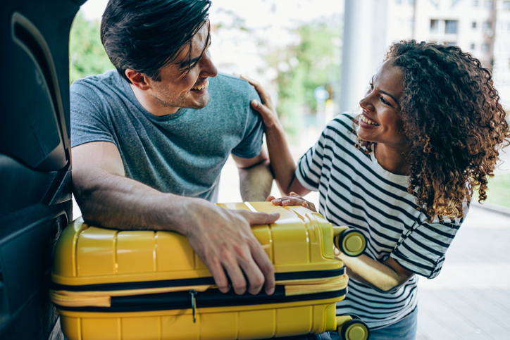 Young couple packing and loading luggage into car trunk for their vacation.