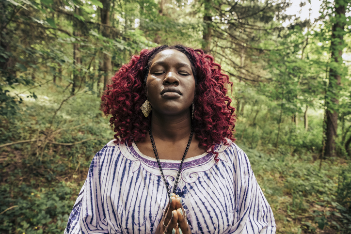 Front facing young woman meditating with eyes closed in woodland area