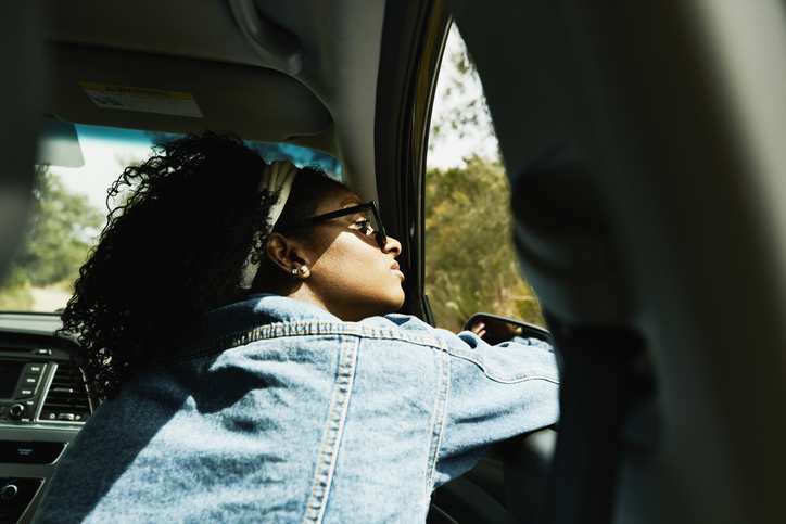 Woman looking out open window of car driving down road