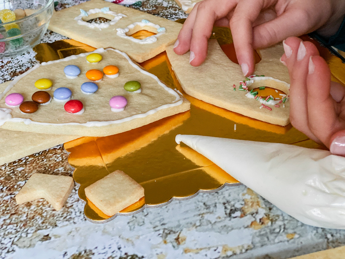 Girl’s hand decorating a gingerbread house at home