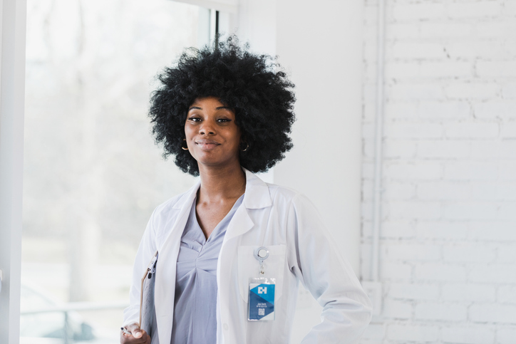 Young adult female intern in lab coat smiles for camera