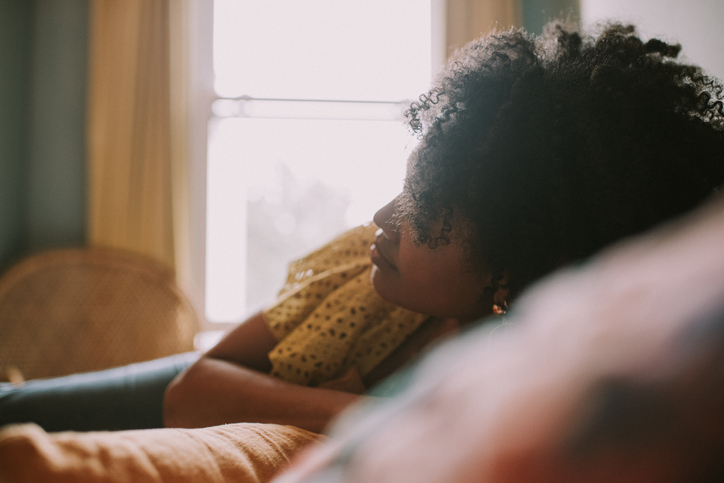 Dreamy image of a young, black woman on a soft bed in a softly lit bedroom