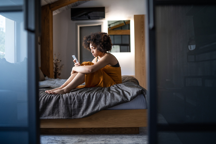 Beautiful afro women sitting on a bed and using smart phone