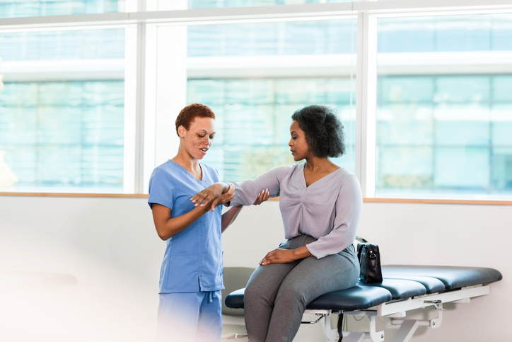Woman watches as physical therapist gently touches her arm