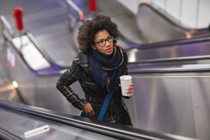 Beautiful young woman with coffee on moving staircase