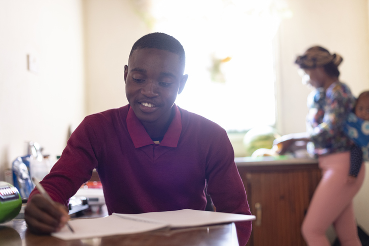 Teenage boy doing homework at kitchen table sister with baby in background